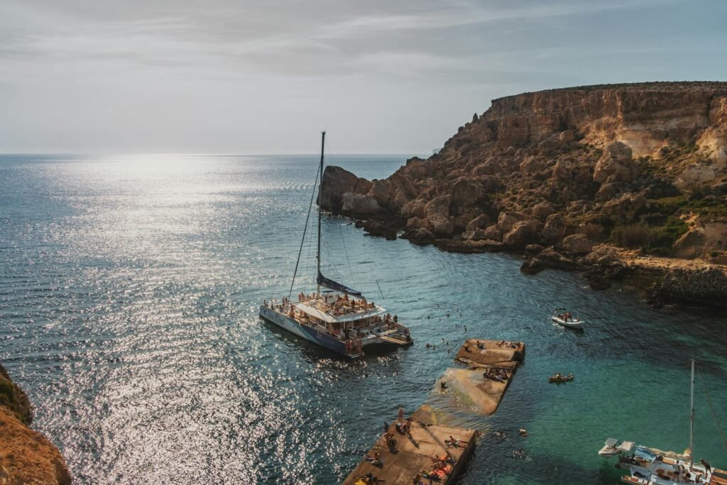 A picturesque coastal bay with yachts and swimmers under a warm sun against dramatic cliffs.