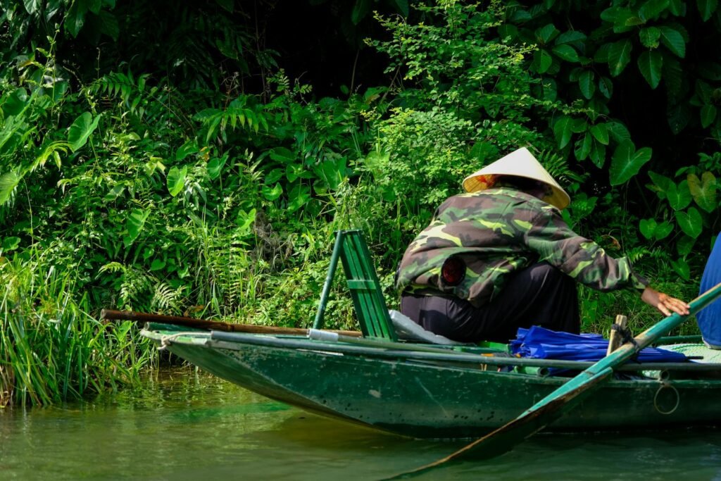 A local navigates a traditional boat through lush greenery in Ninh Binh, Vietnam.