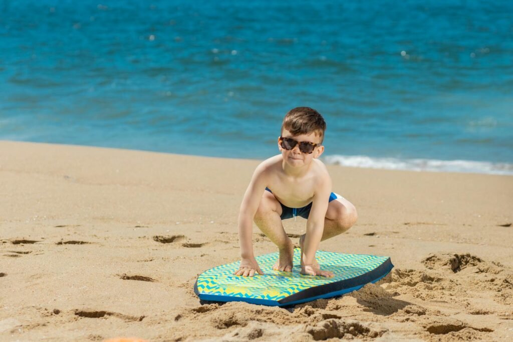 A young boy wearing sunglasses prepares to surf on a sunny beach day.